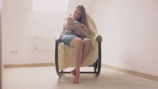 Madre sonriendo al hijo recién nacido arrullándolo en una mecedora. 4k — Vídeos de Stock