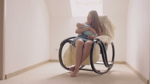 Мать улыбается новорожденному сыну, усыпляя его в кресле-качалке. 4k — стоковое видео