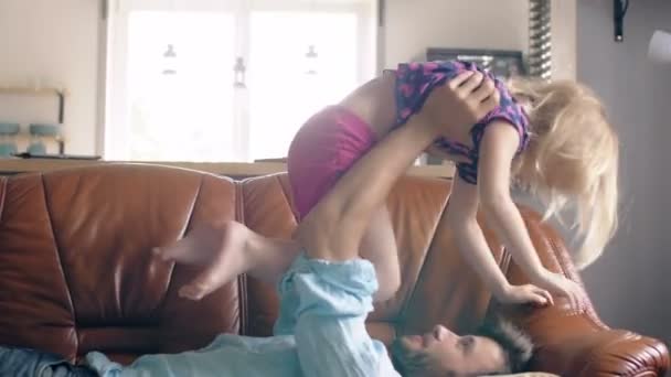 Um jovem pai e uma linda filhinha feliz estão brincando no sofá da sala de estar. 4k — Vídeo de Stock