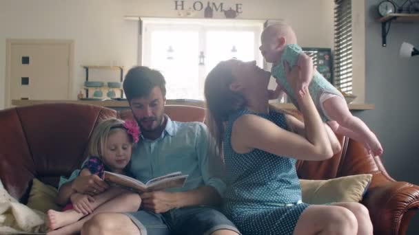 Une famille de quatre personnes est assise sur le canapé et parle. maman tient son adorable bébé souriant. 4k — Video