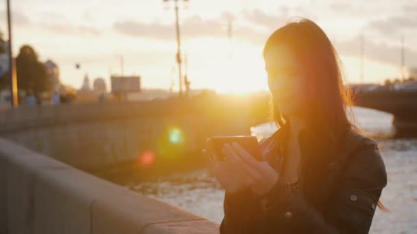 Ung vacker flicka tar selfie på bakgrunden av bron i ljusa strålar från solen. 4k — Stockvideo