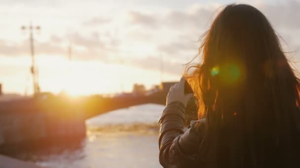 Krásná mladá dívka dělá smartphone Foto mostu v zářivé paprsky zapadajícího slunce. 4k — Stock video