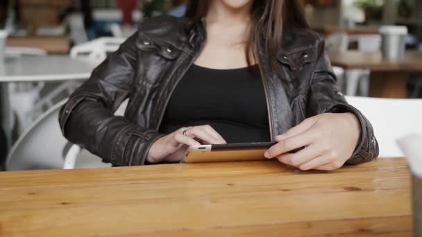 Jovem elegante usa um tablet envia sms sentado a uma mesa no café moderno, maravilhas, sorrindo . — Vídeo de Stock