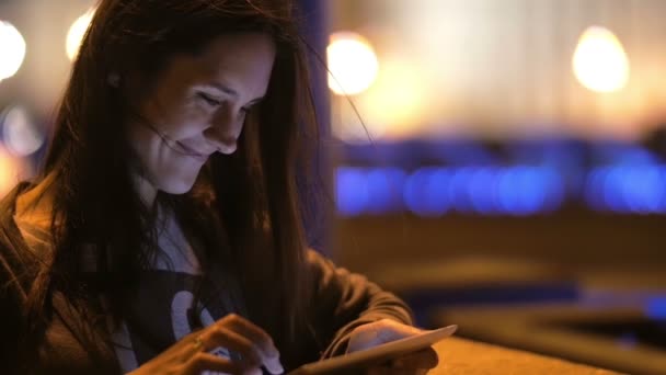 Una bella giovane donna che usa il suo tablet di notte. Sorride, il vento soffia i capelli, sfondo sfocato, lento mo — Video Stock