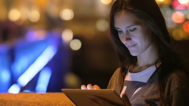 美しいブルネットの女性、彼女のタブレットを使用しています。夜の街の遅い mo 背景にぼやけライト — ストック動画