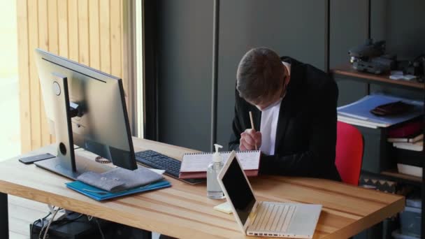 Młody, profesjonalny, biały biznesmen pracujący sam przy nowoczesnym stole biurowym w masce ochronnej COVID-19. — Wideo stockowe