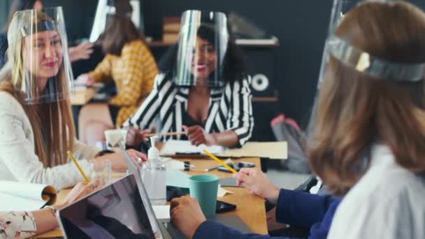 Las mujeres trabajan juntas en la oficina moderna después del cierre de COVID-19. Hermoso feliz diversos colegas con escudos faciales. — Vídeos de Stock