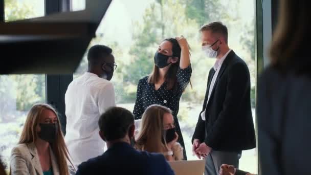 Groupe de jeunes gens d'affaires souriants heureux parlant, travaillant dans un bureau moderne, tous portant des masques de sécurité COVID-19. — Video