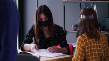 Güzel beyaz iş kadınları COVID-19 maske ve yüz maskesi takarak ofis masasında birlikte çalışır ve konuşurlar..