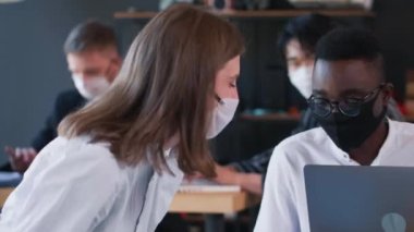 Ofiste maske takarak çalışan mutlu, genç şirket yöneticileri. İş yerinde COVID-19 tıbbi koruma.