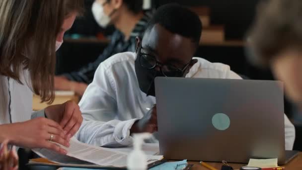 Trabalho em equipe no escritório moderno após a crise COVID-19. Jovens empresários multiétnicos felizes trabalham à mesa com máscaras. — Vídeo de Stock