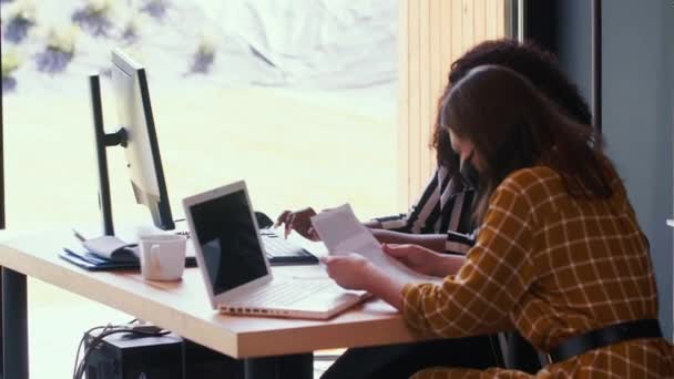 Schöne multiethnische Geschäftsfrauen arbeiten mit Dokumenten und Laptops am Bürotisch und tragen COVID-19-Masken. — Stockvideo