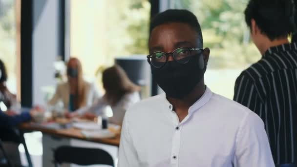 Porträt eines jungen, ernsthaften, smarten Studenten der 20er Jahre mit Brille, der im Büro in Zeitlupe eine Gesichtsmaske trägt — Stockvideo