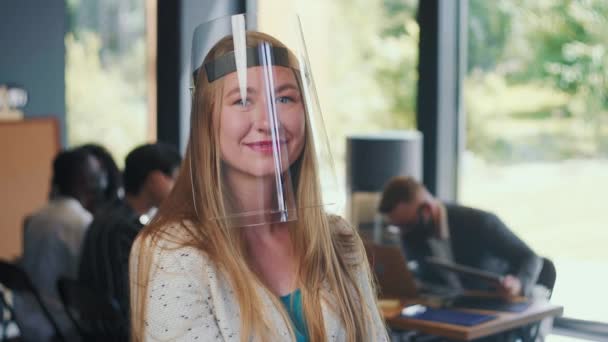 Sécurité au travail au bureau sur COVID-19. Portrait de jeune femme d'affaires souriante en plastique transparent face shield slow motion. — Video