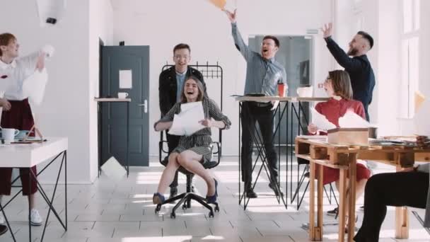 RED EPIC-W Feliz sonriente mujer de negocios rubia divirtiéndose con colegas de oficina tirando papel en la silla de cámara lenta. — Vídeo de stock