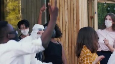 COVID-19 karantinasından sonra normal hayatın tadını çıkarıyorum. Mutlu çoklu etnik arkadaşlar partide maske ve takım elbiseyle dans eder..