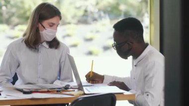 COVID-19 'dan sonra tıbbi maske takarak ofiste birlikte çalışan iki mutlu iş adamı..