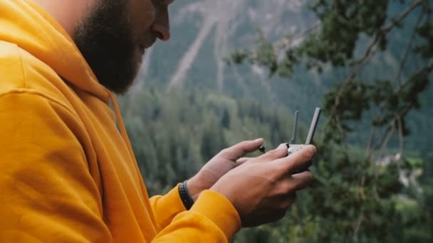 Młody szczęśliwy casual brodaty wideograf człowiek w żółtej bluzie kontroli drone samolotów z pilotem w jesiennych górach. — Wideo stockowe