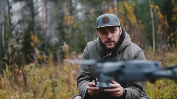 Junger glücklicher lässiger bärtiger kaukasischer Kameramann steuert Drohnen-Kameraflugzeug mit Fernbedienung im Herbstwald. — Stockvideo