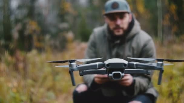 Drohnen-Kameraflugzeug aus nächster Nähe wird von einem jungen glücklichen, bärtigen kaukasischen Kameramann im herbstlichen Wald gesteuert. — Stockvideo