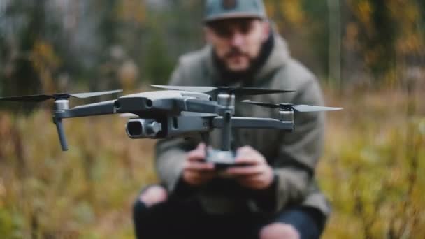 Närbild drönare kamera flygplan vrida, flyger upp kontrolleras av unga glada kaukasiska videograf man i höstskogen. — Stockvideo