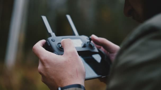 Close-up achteraanzicht mannelijke handen besturen drone vliegtuigen met behulp van moderne afstandsbediening met smartphone in de herfst bos. — Stockvideo