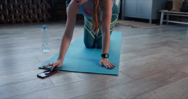 迷人的金发年轻女子在家里用智能手机做健身锻炼，以保持健康的自我封闭状态. — 图库视频影像