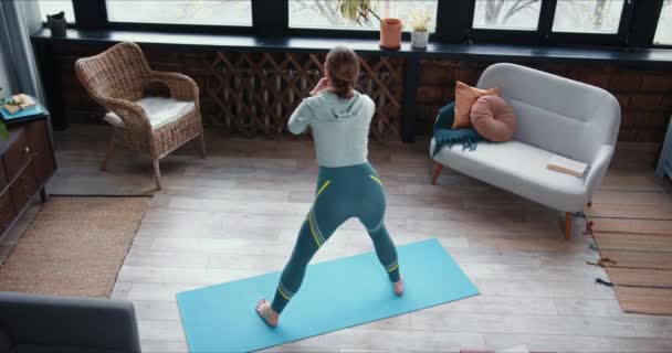 Achteraanzicht hoge hoek sportieve slanke jonge vrouw doet fitness workout been oefeningen op yoga mat thuis op quarantaine. — Stockvideo