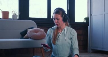 Güzel, sportif, genç, sarışın bir kadın evde meditasyon yapıyor. Kendini izolasyon üzerine akıllı telefon müzik uygulaması kullanıyor..