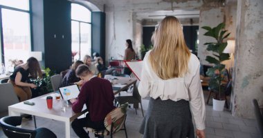 Arkadan bakıldığında, kendine güvenen genç, sarışın patron iş arkadaşlarıyla çok ırklı çatı katında ağır çekimde buluşuyor..