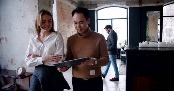Happy young Asian coach business man and Caucasian woman walk along modern busy loft office using tablet slow motion.