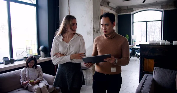 Gelukkig jong aziatisch coach zakenman en blanke vrouw lopen langs moderne drukke loft kantoor met behulp van tablet slow motion. — Stockfoto