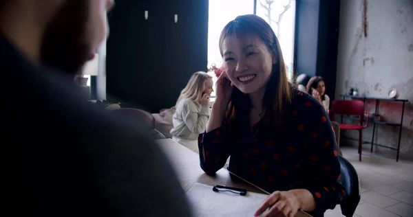 Happy excited smiling Asian woman takes a job interview in light multiethnic office, talking to male HR slow motion.