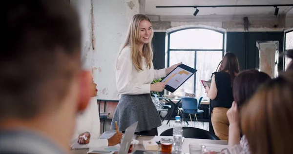 Joven hermosa rubia feliz gen-z entrenador femenino utilizando la tableta para presentar los datos en la reunión de equipo de oficina multiétnica moderna. — Foto de Stock