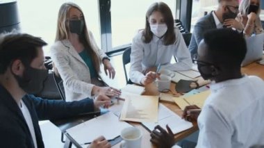 Yüksek açılı, etnik çeşitliliğe sahip yaratıcı girişim insanları, açık modern ofis masasında çalışan maskeler takıyorlar..