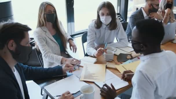 Høyvinklet, multietnisk kreativ nyetablering - folk bruker masker på å møtes ved det moderne kontorbordet. – stockvideo