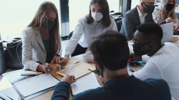 Novas normas de segurança no local de trabalho. Feliz positivo diversos empresários cooperam em reunião de mesa de escritório usando máscaras. — Vídeo de Stock