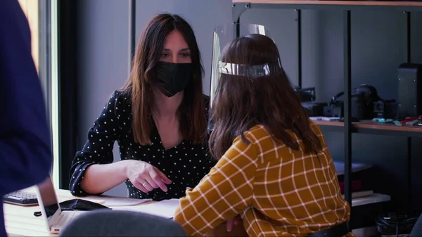 Jovens mulheres de negócios caucasianas bonitas trabalham e conversam juntas na mesa de escritório usando máscara COVID-19 e protetor facial. — Fotografia de Stock