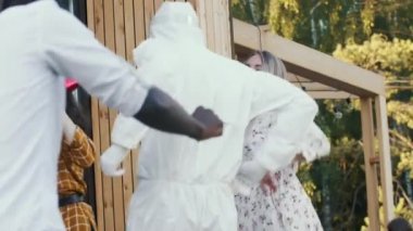 Yakın çekim heyecanlı çoklu etnik arkadaşlar destansı eğlence partisinde tıbbi güvenlik maskeleri, yüz kalkanları ve kıyafetlerle dans ediyorlar..