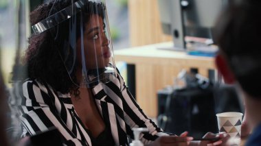 Genç, çekici, başarılı, siyah iş kadını modern ofis masası toplantısında COVID-19 yüz maskesi takıyor..