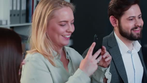 Emocionada rubia sonriente mujer de negocios caucásica toma la foto del teléfono inteligente sentado en la reunión del equipo de oficina loft multiétnico. — Vídeos de Stock