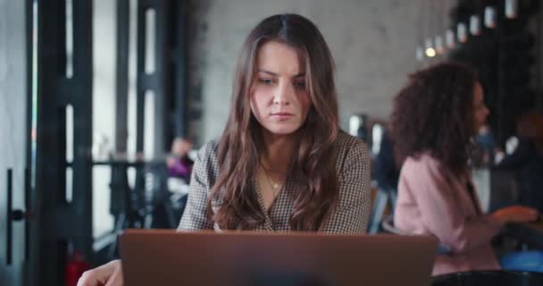 Portrait of young serious Caucasian brunette female IT freelancer using laptop to work online at busy loft coworking. — Stock Video