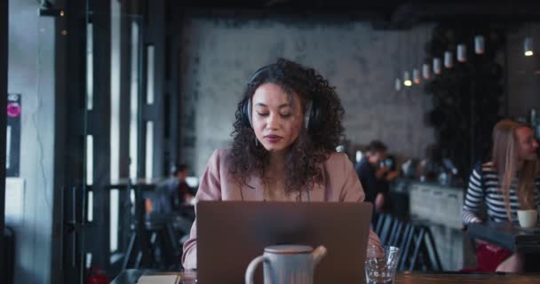 Concept de travail indépendant. Jeune écrivain créative multiethnique heureuse regarde à droite en utilisant un ordinateur portable travaillant dans un café à la mode. — Video