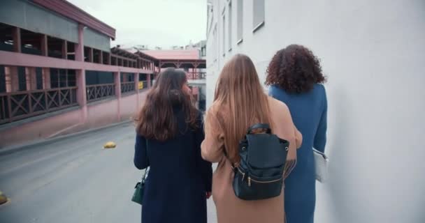 Plan cinématographique de trois belles jeunes amies joyeux bavarder joyeusement tout en marchant le long du mur de construction de la ville. — Video