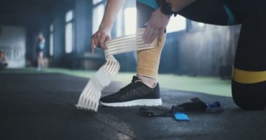 Yakın plan kadın çapraz formda sporcu, modern spor salonunda ağırlık kaldırma egzersizine hazırlanmak için bacağına elastik diz bağlıyor..