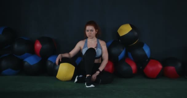 Girl-Power-Konzept. Zoom im Porträt einer jungen schönen Sportlerin, die müde auf dem Boden des Fitnessstudios sitzt und in die Kamera blickt. — Stockvideo