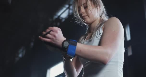 Baixo ângulo jovem bela atleta de levantamento de peso feminino coloca tiras de pulso, preparando-se para o exercício na academia moderna. — Vídeo de Stock