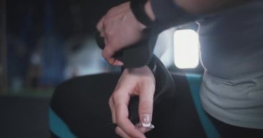 Spor salonunda egzersiz yapmadan önce çapraz formda sporcu kadın ağırlık kaldırma bilekliklerini ellerine takar ve kalkıp uzaklaşır..