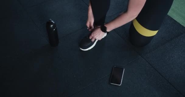 Sportkleding en accessoires. Vrouwelijke atleet strikken sneaker veters voor het sporten met smart phone en waterfles. — Stockvideo