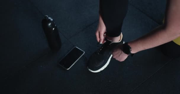 Equipamento e equipamento de fitness. Mulher desportiva amarra atacadores antes do treino de ginástica com telefone inteligente e garrafa de água. — Vídeo de Stock